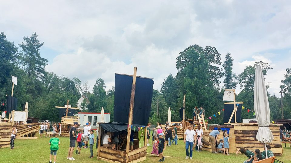 Viele Kinder und Jugendliche inmitten von selbstgebauten Holzgebäuden auf einer Wiese