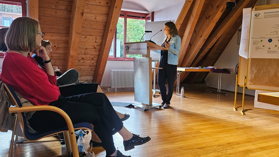 Frau steht am Renderpult des Landratsamts, hinter ihr stehen Pinnwände mit Plakaten. Das Publikum hört zu.