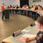 Ein Sprecher an einem Pult und die Jugendlichen sitzen in einem Halbkreis an Tischen im Plenum