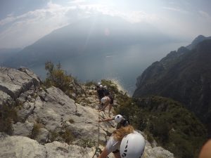 Menschen an einem Kletterseil über dem Gardasee bei Sonnenschein