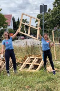 Zwei Pädagoginnen recken halten eine Holzpalette in die Luft und freuen sich